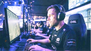 Koncentrált profi e-sport játékos fejhallgatóban, billentyűzettel és egérrel a monitor előtt egy ESL bajnokságon